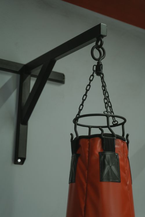 Free Close-up of a red punching bag suspended on a metal frame in a gym, showcasing fitness equipment. Stock Photo