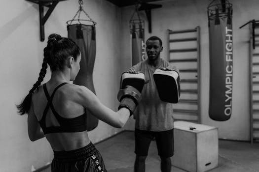 A female boxer trains with a coach using focus mitts in a gym setting, emphasizing technique and power.