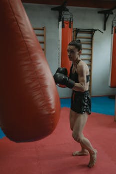 Focused female boxer practicing in a gym with a punching bag.