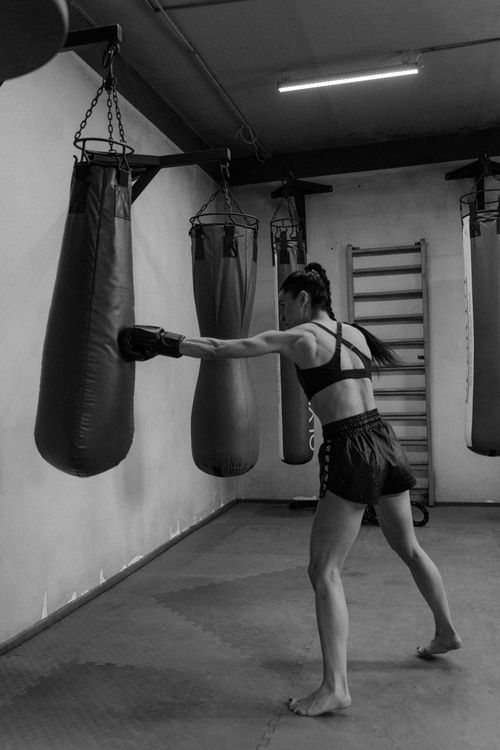 Free Woman practicing boxing by punching a bag in a gym. Black and white photo shows intense training. Stock Photo
