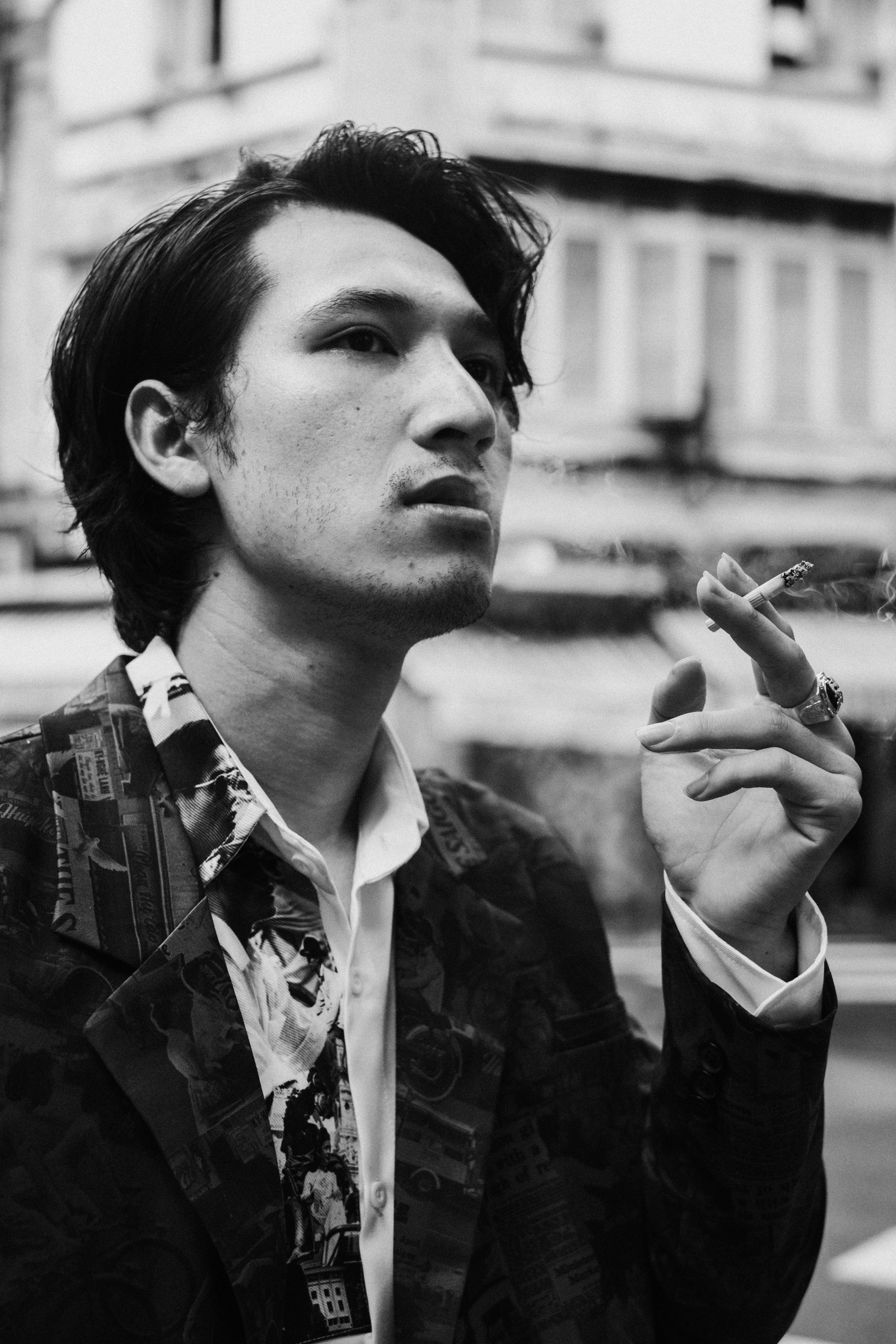 pensive young ethnic man smoking cigarette on city street