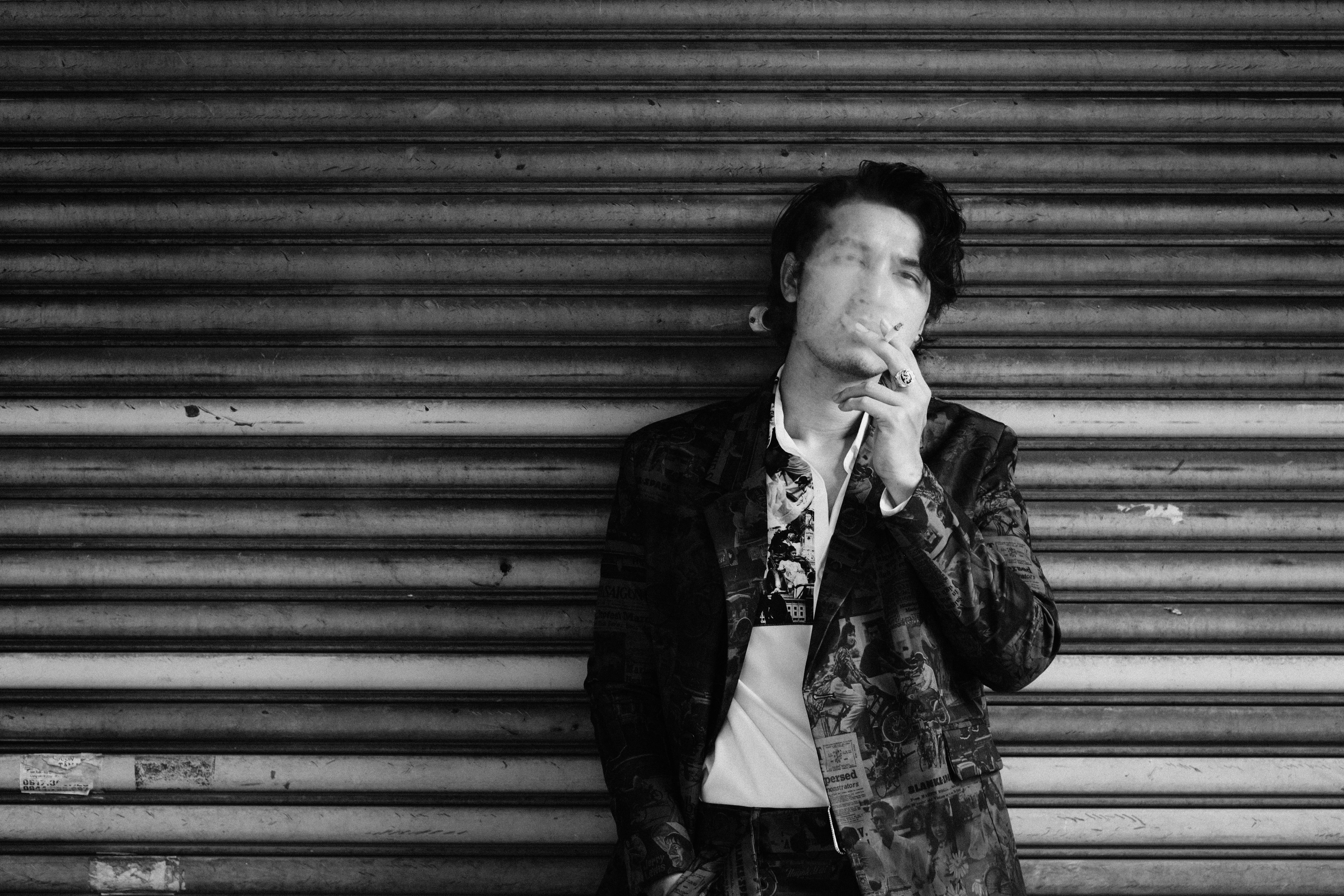 thoughtful young ethnic guy smoking cigarette near shabby wall