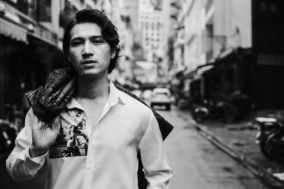 Black and white of self esteem young ethnic male holding blazer over shoulder while relaxing on street in city old district