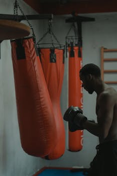 A dedicated boxer practicing with punching bags in a dimly lit gym.