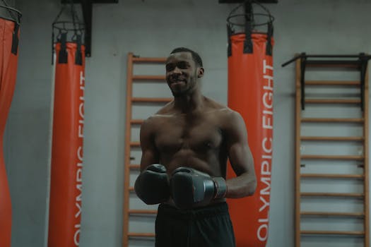 Shirtless muscular athlete in a gym preparing for boxing with gloves. Focuses on strength and fitness.