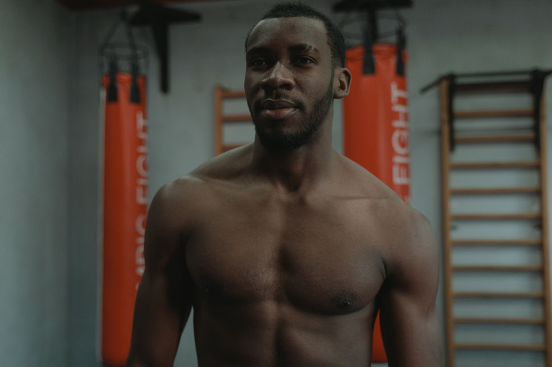 Muscular man in gym with punching bags, emphasizing fitness and strength.