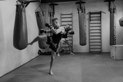 Dynamic action scene of men training with punching bags in a monochrome gym setting.