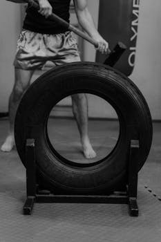 A monochrome image of a man training with a sledgehammer in a gym, focusing on strength.