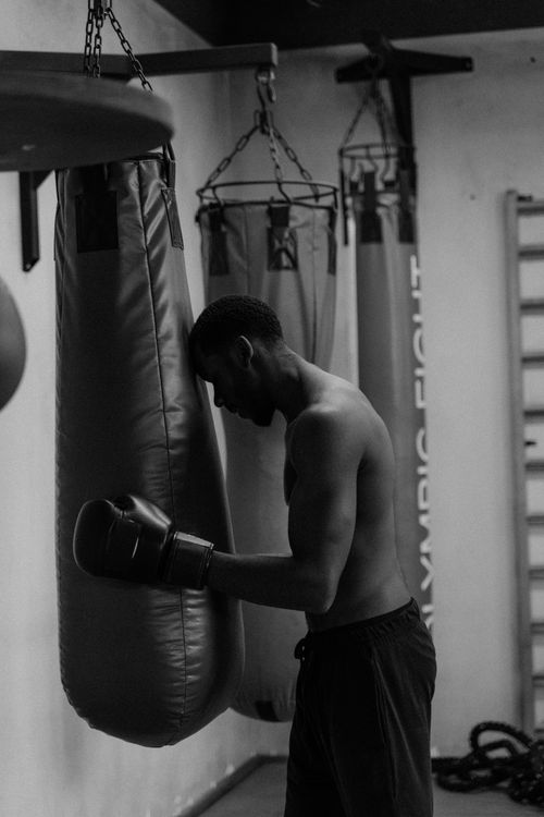 Free A shirtless boxer leans on a punching bag, showcasing strength in a gym setting. Stock Photo