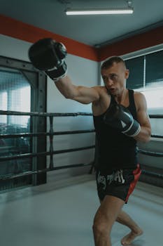 Male boxer practicing shadow boxing in a gym with gloves and tank top.