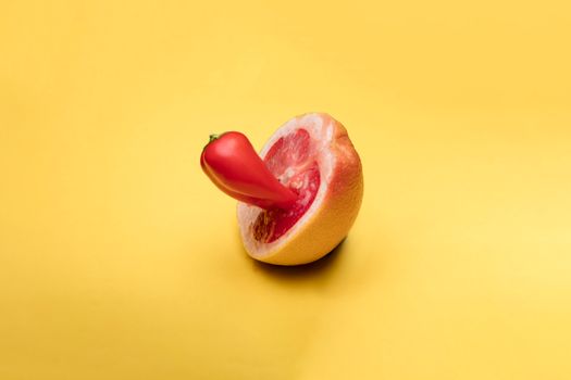 Conceptual artwork featuring a grapefruit with a red pepper on a vibrant yellow background.