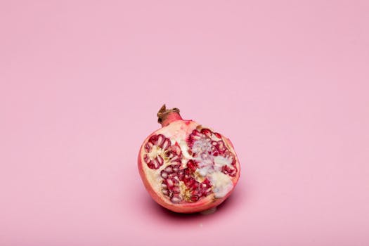 A close-up of a ripe pomegranate on a pink background, showcasing its vibrant seeds and natural texture.