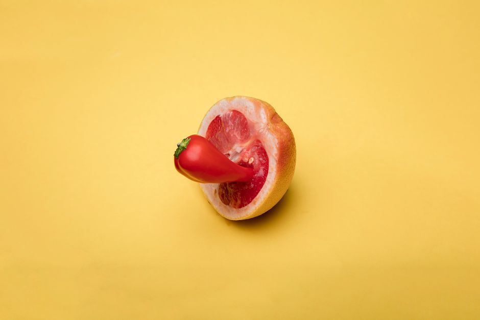 A red pepper embedded in a halved grapefruit on a yellow background, showcasing a vibrant conceptual art style.