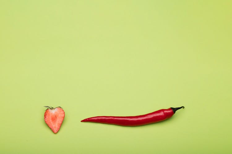 Chili Pepper And Half Of A Strawberry Against Green Background