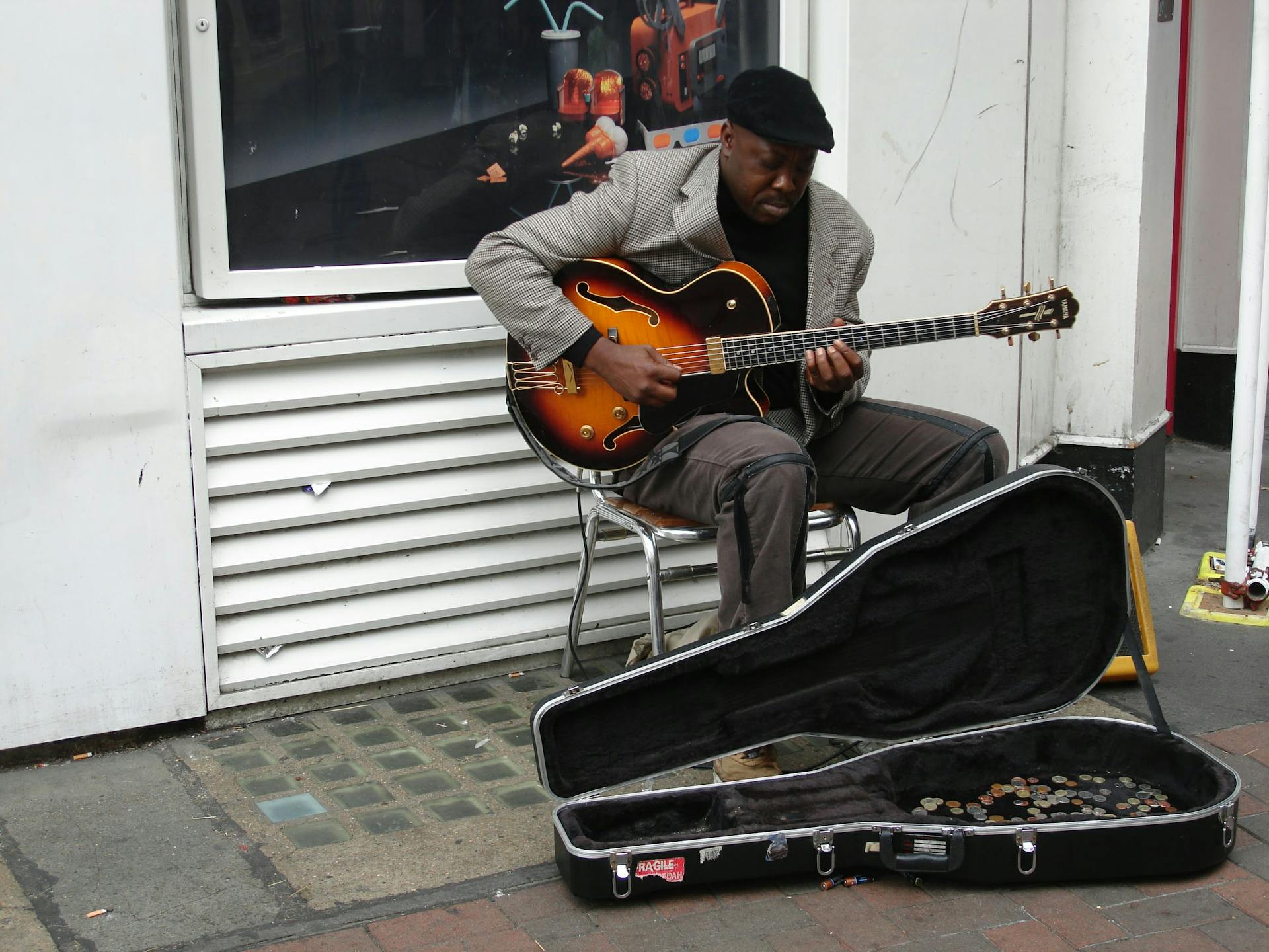 Man in a Black Hat Playing Guitar on a Pavement