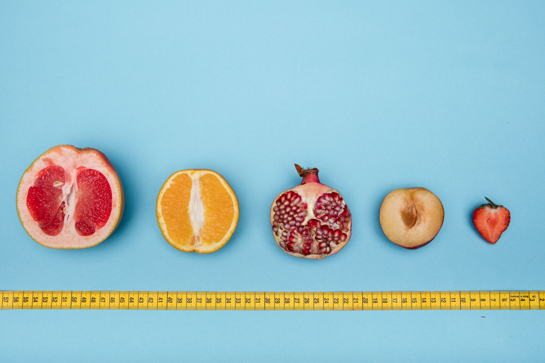 Colorful halved fruits lined up against a light blue background with measuring tape, perfect for healthy lifestyle themes.
