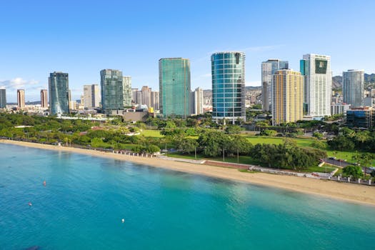 Aerial view of Honolulu's beachfront skyscrapers with clear blue ocean on a sunny day.