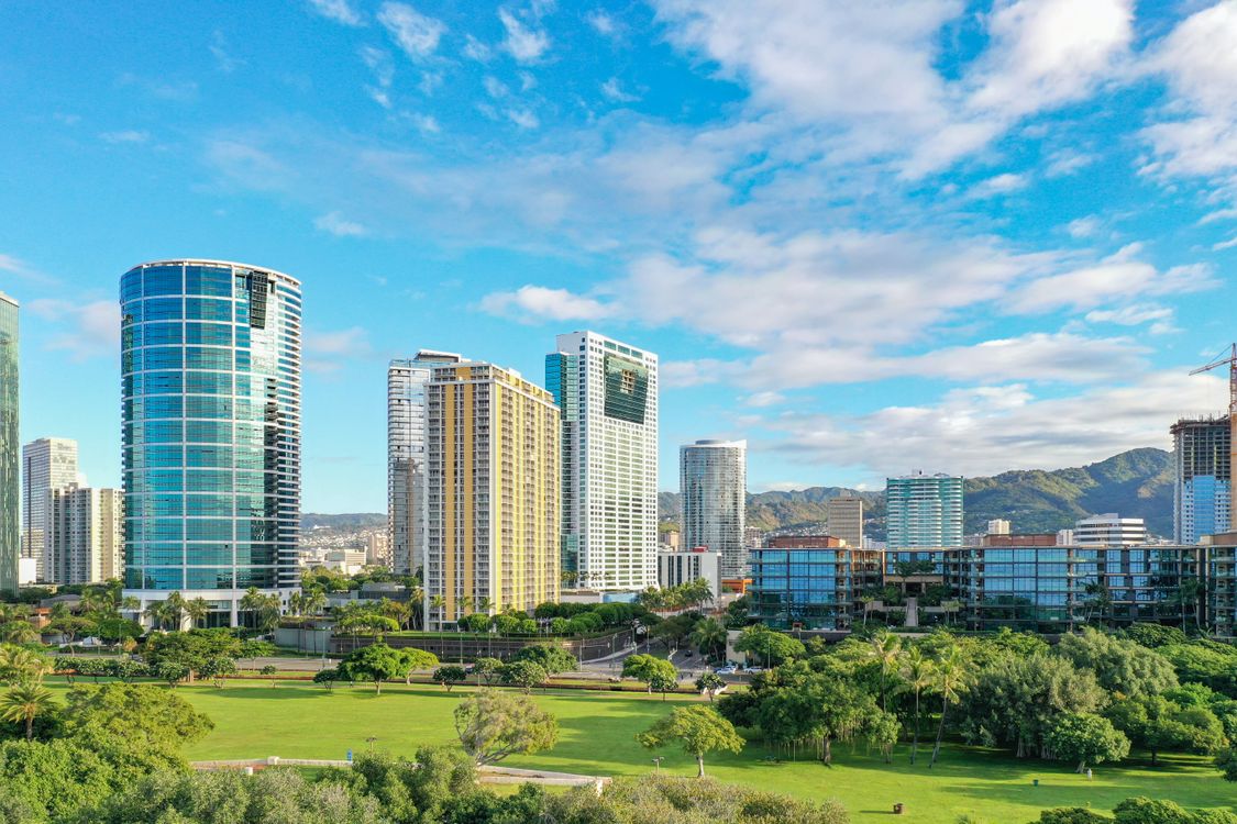 Green Grass Field Near City Buildings Under Blue Sky · Free Stock Photo