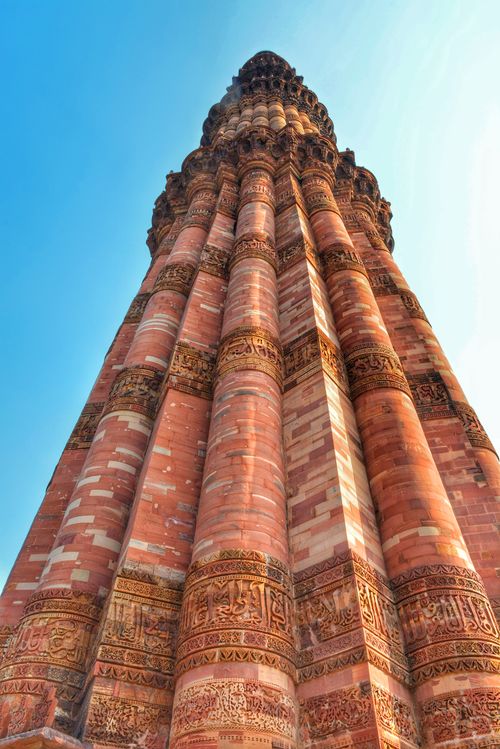 Free Dramatic low-angle shot of Qutub Minar showing intricate red brickwork against a blue sky. Stock Photo