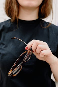A woman in a black shirt holding eyeglasses, focusing on eyewear fashion.