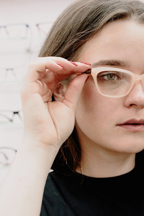 Crop young female client putting on eyewear while choosing new rim glasses in salon