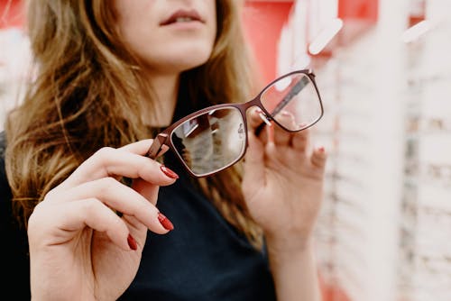 Free Crop female client with stylish glasses in hands picking glasses rim in optical salon Stock Photo