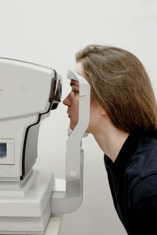 Free Side view of female client putting head on medical machine for checking eyesight in contemporary clinic Stock Photo