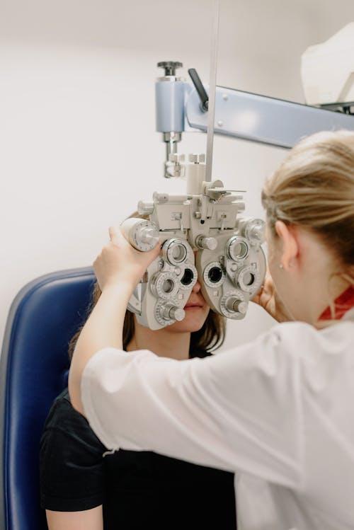 Anonymous optometrist wearing medical uniform calibrating optical phoropter while examining vision of patient in modern clinic with special equipment during work