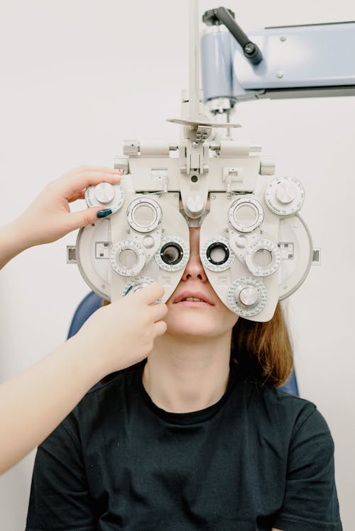 Unrecognizable ophthalmologist using professional phoropter equipment to check eyesight of patient sitting in cabinet against white wall in modern clinic