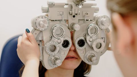 Unrecognizable female ophthalmologist adjusting medical equipment while doing vision check up of patient in contemporary clinic during work