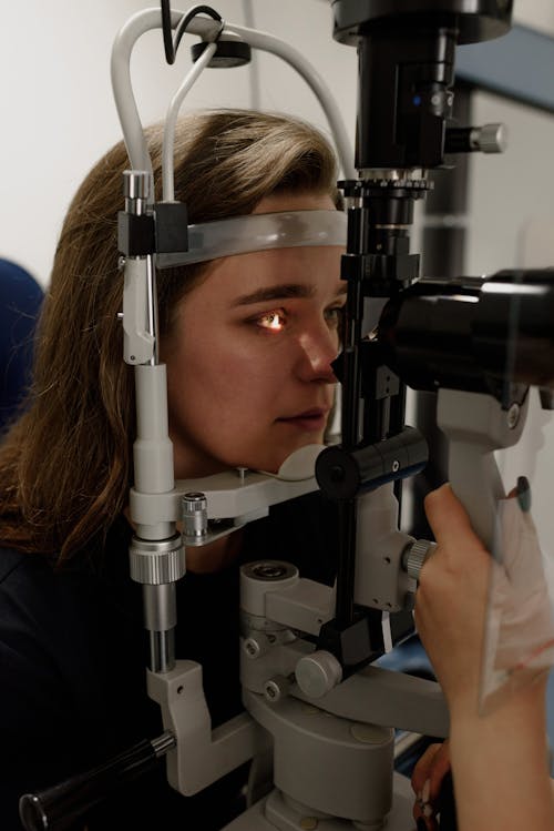 Side view of female patient sitting at ophthalmic microscope with light near crop oculist while examining eyesight in professional clinic