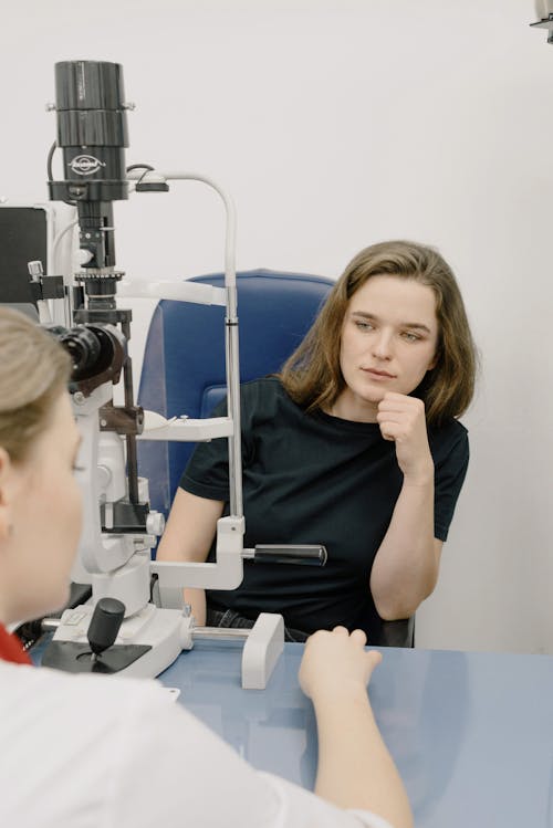 Crop oculist at table with microscope and patient