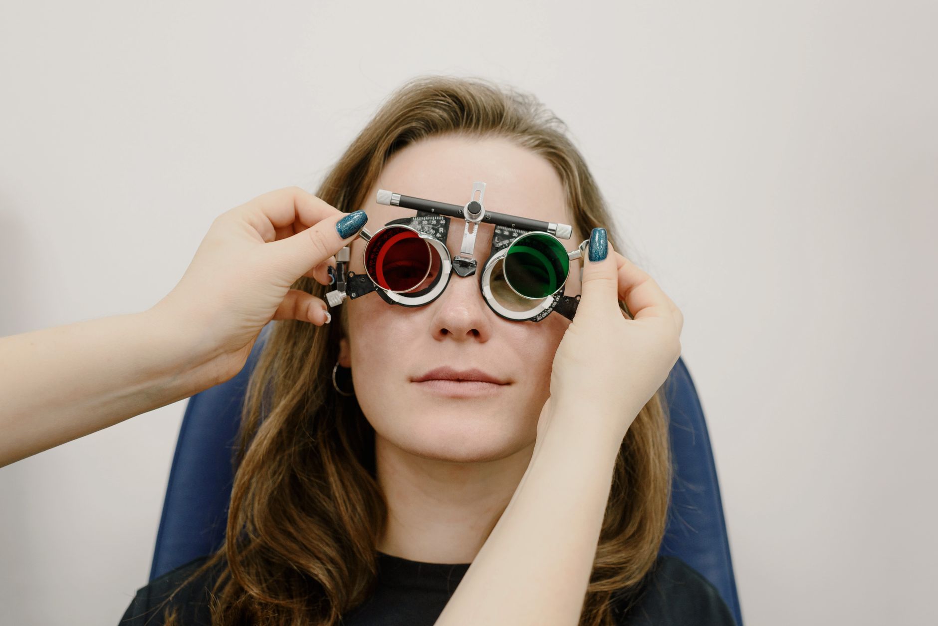 Unrecognizable female doctor correcting ophthalmic glasses selecting lenses on eyes of female patient during appointment in clinic against white wall