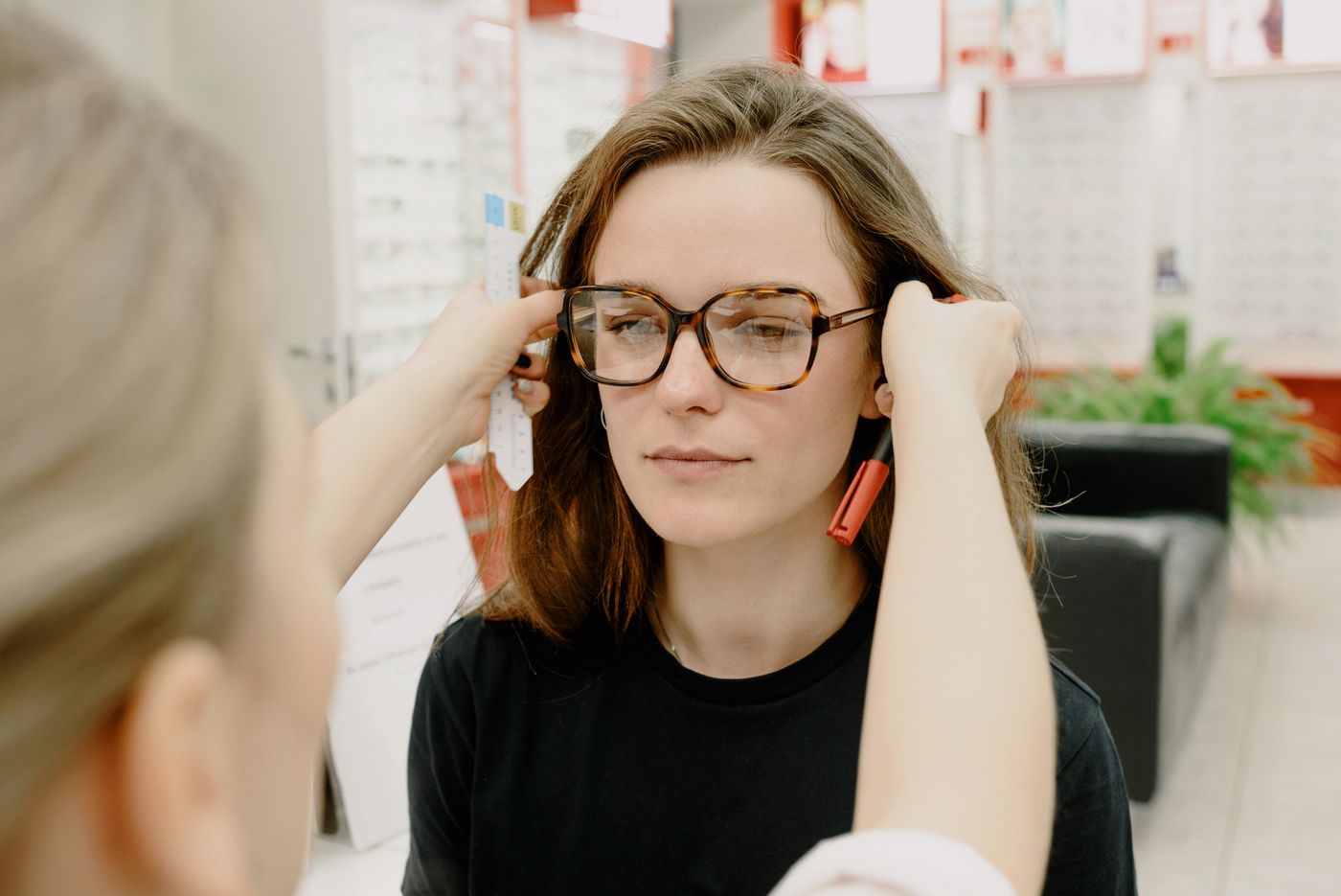 An optician fitting eyeglasses on a woman
