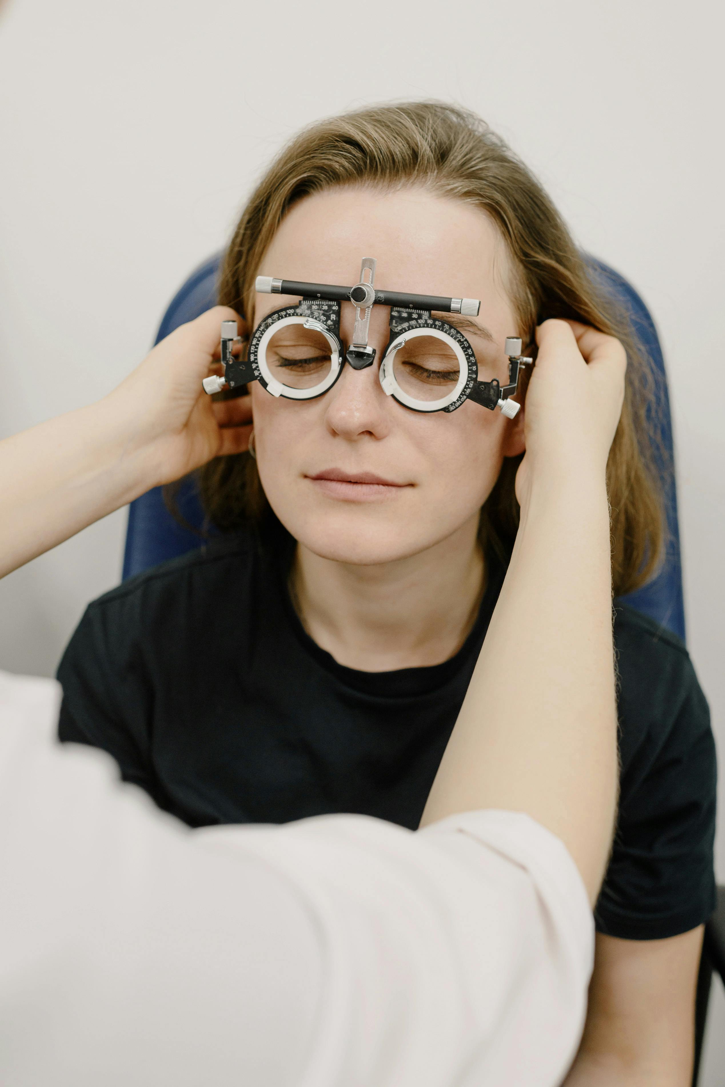 Unrecognizable medic adjusting phoropter with diopters on eyes of female patient while doing vision check up in clinic during appointment