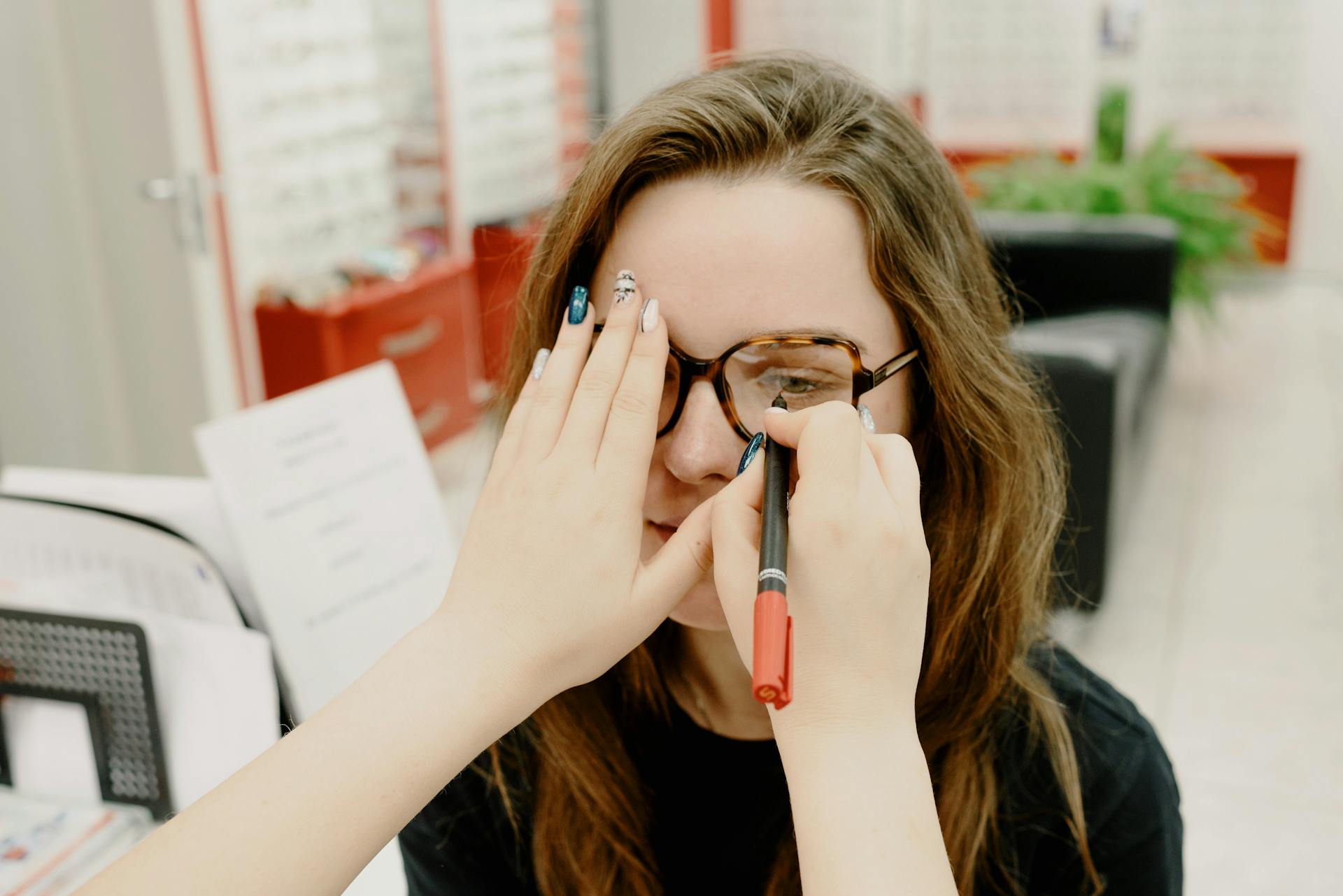 Anonymous female doctor covering eye of female client while choosing proper lenses during appointment in optical salon on blurred background