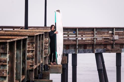 Photo of a Man in a Black Wetsuit Holding His Surfboard