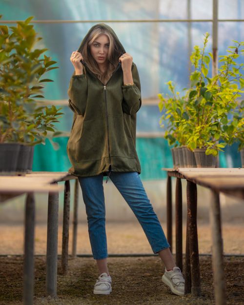 Free Stylish woman in a hoodie poses among plants in a greenhouse, showcasing a relaxed vibe. Stock Photo