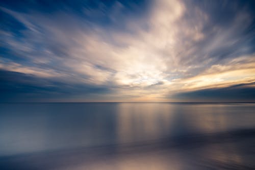 Picturesque seascape of cloudy sunset sky over smooth endless sea with reflecting surface in evening