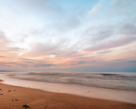 Wavy sea washing sandy shore under endless tranquil sunny cloudy sky in daytime