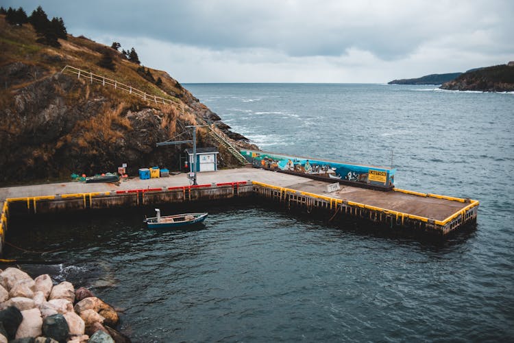 Old Pier In Stormy Rocky Ocean Against Overcast Sky