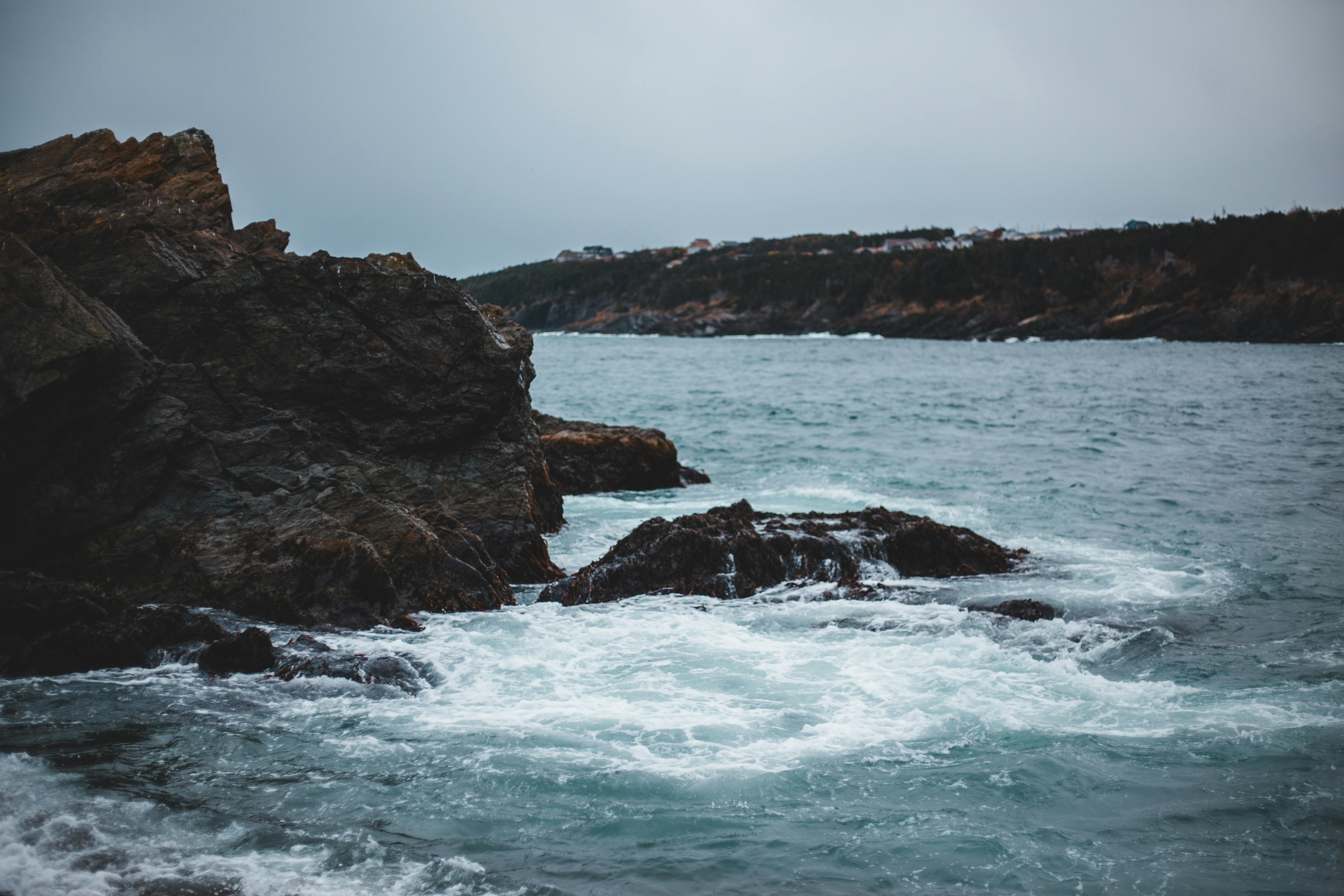 Explore a scenic rocky coastline with powerful waves crashing against the cliffs under an overcast sky.