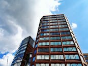 现代摩天大楼的低角度视图，玻璃立面映衬着明亮的蓝天和白云