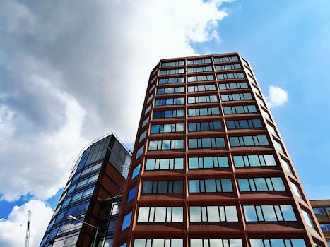 现代摩天大楼的低角度视图，玻璃立面映衬着明亮的蓝天和白云