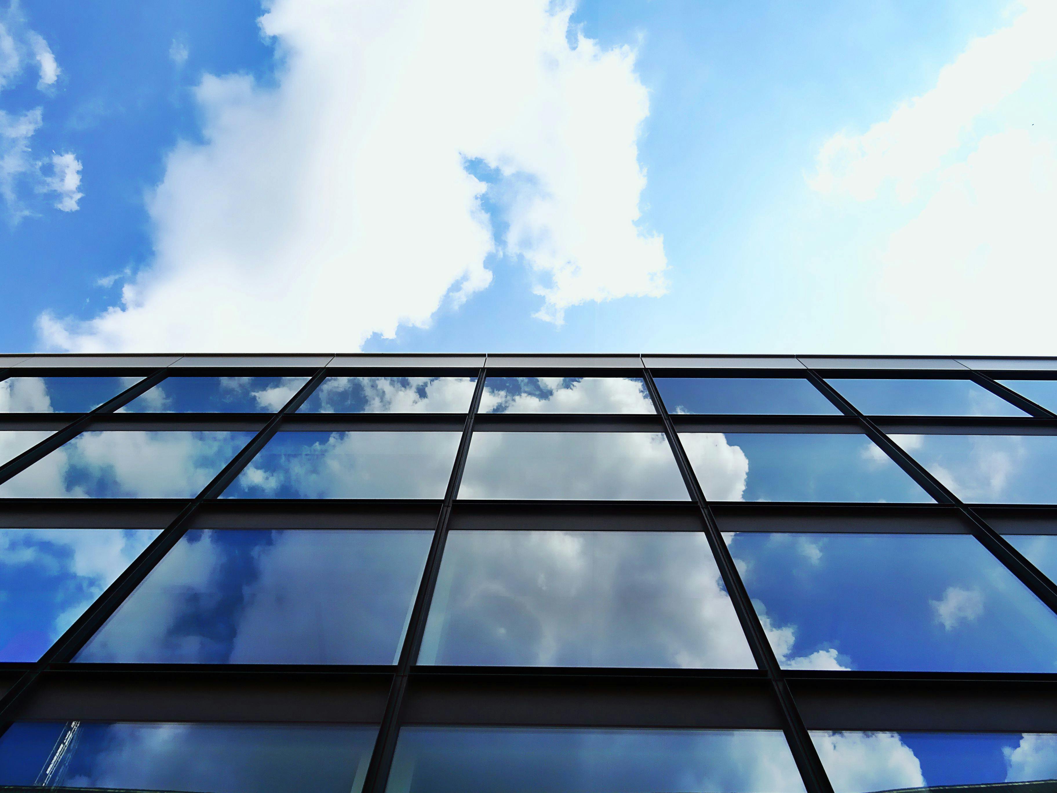 蔚蓝天空下，低角度视角中云层倒映在现代摩天大楼的玻璃立面上
