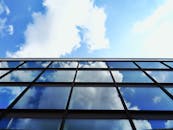 蔚蓝天空下，低角度视角中云层倒映在现代摩天大楼的玻璃立面上