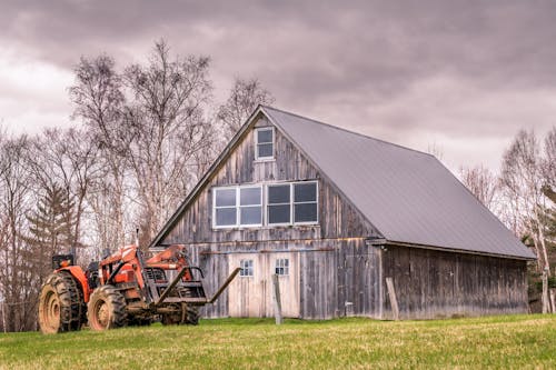Free Tractor parked near wooden shack on grassy terrain in village Stock Photo