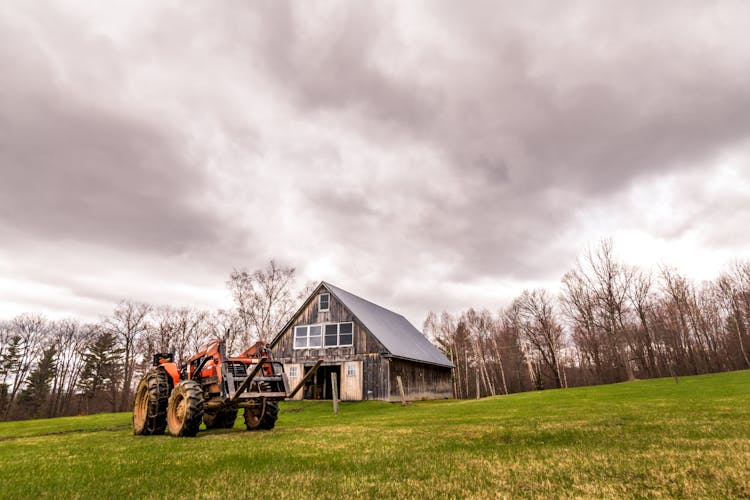 Wooden Barn With Tractor In Farm Under Cloudy Sky