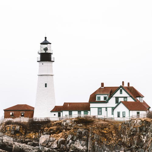 Aged lighthouse and typical residential cottages or rocky coast under overcast sky