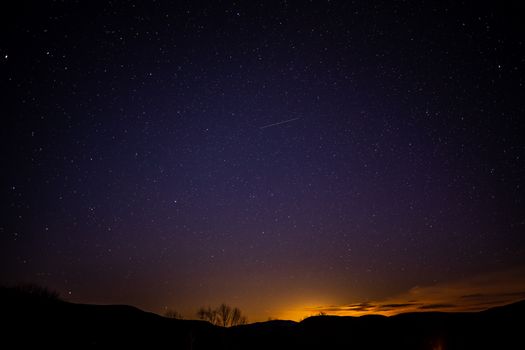 夜晚，树木和小山的剪影与如画的星空构成了一幅惊人的风景